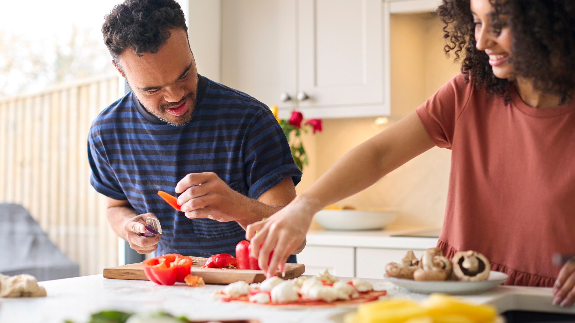 Couple At Home With Man With Down Syndrome And Woman Preparing Topping For Pizza In Kitchen Together