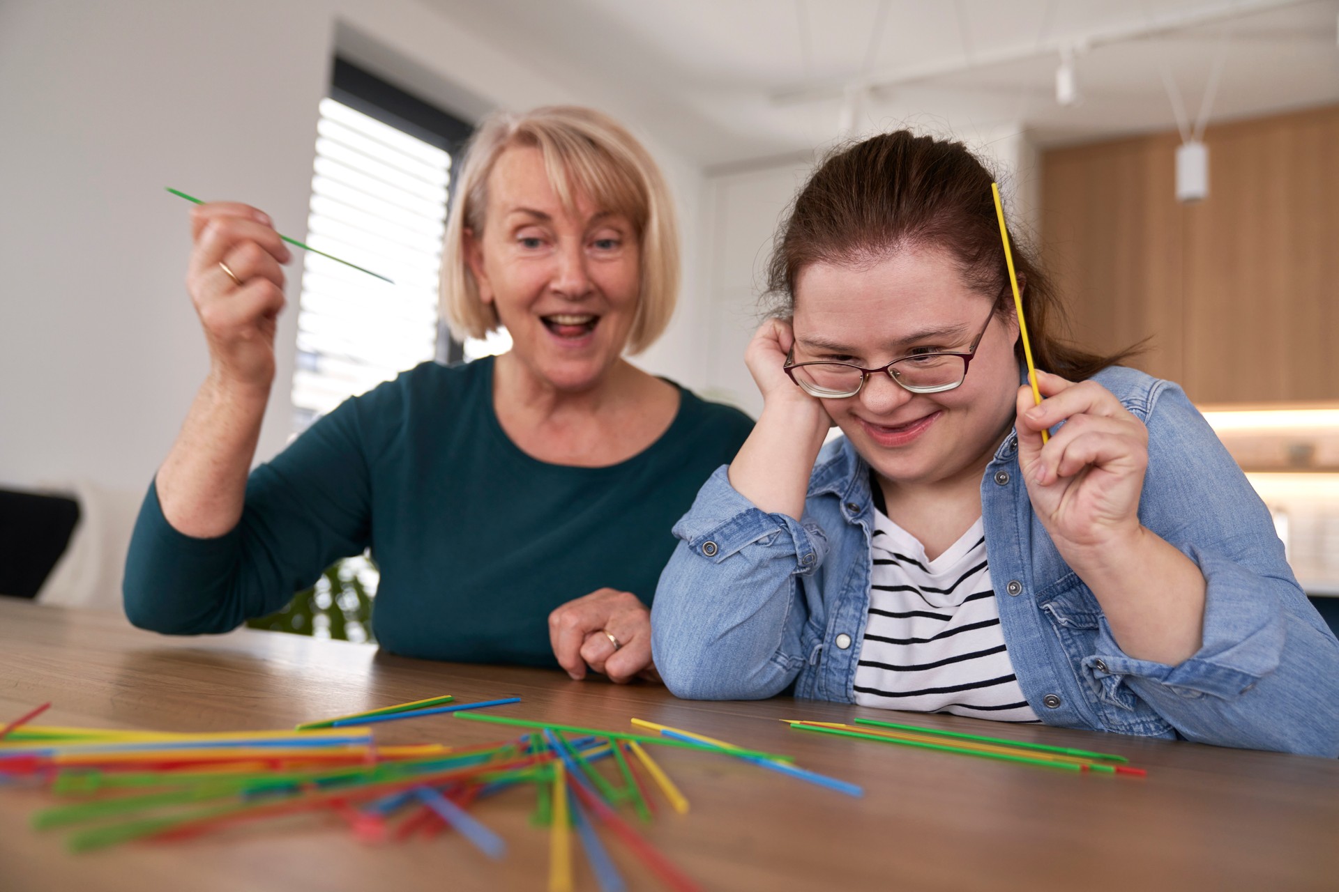 Down syndrome woman and her mother playing pick up sticks at home